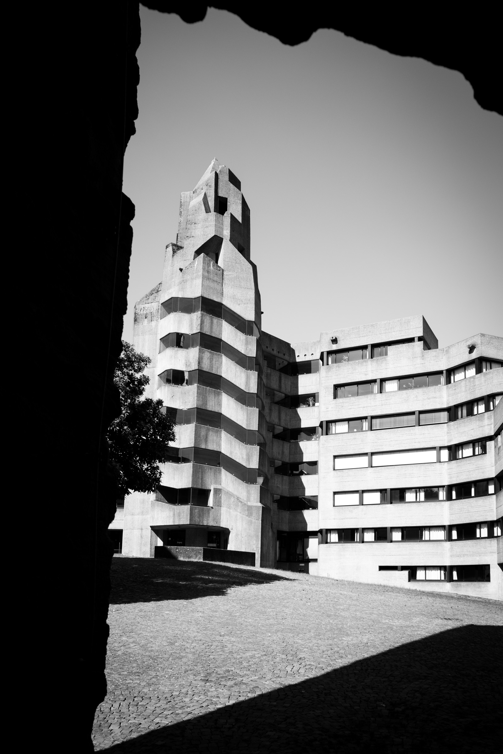 Concrete tower of Rathaus Bensberg seen through a dark stone archway, cobblestone courtyard in foreground