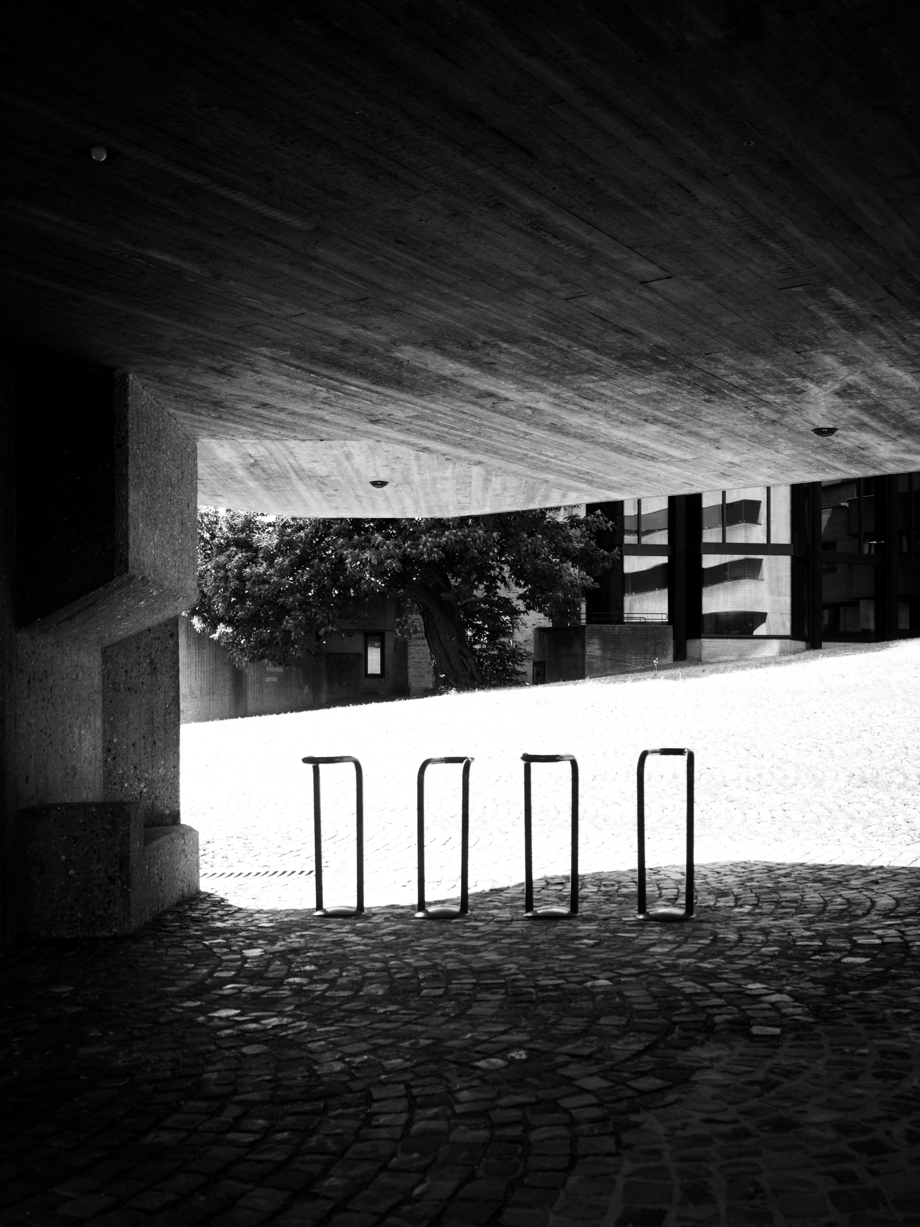 View from under a concrete overhang toward bike racks and a sunlit courtyard