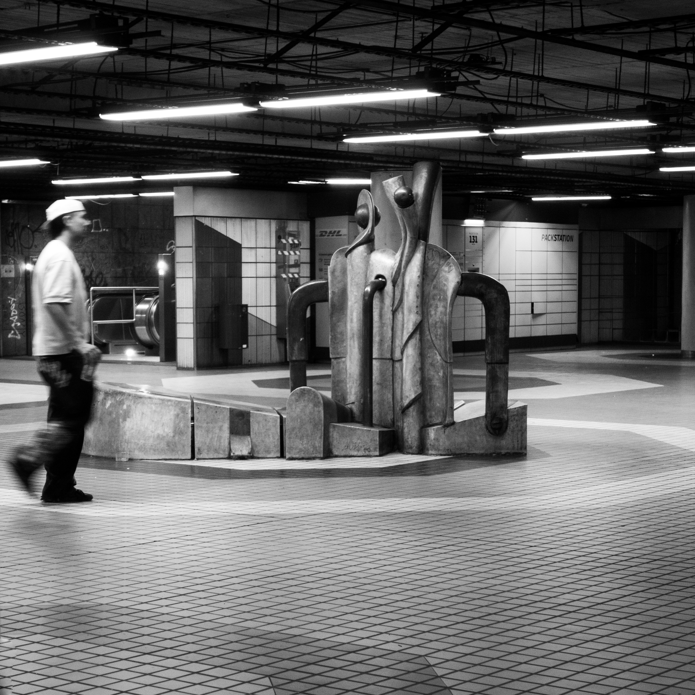 Abstract sculpture in the underground concourse at Friesenplatz, Cologne, with a passerby in motion