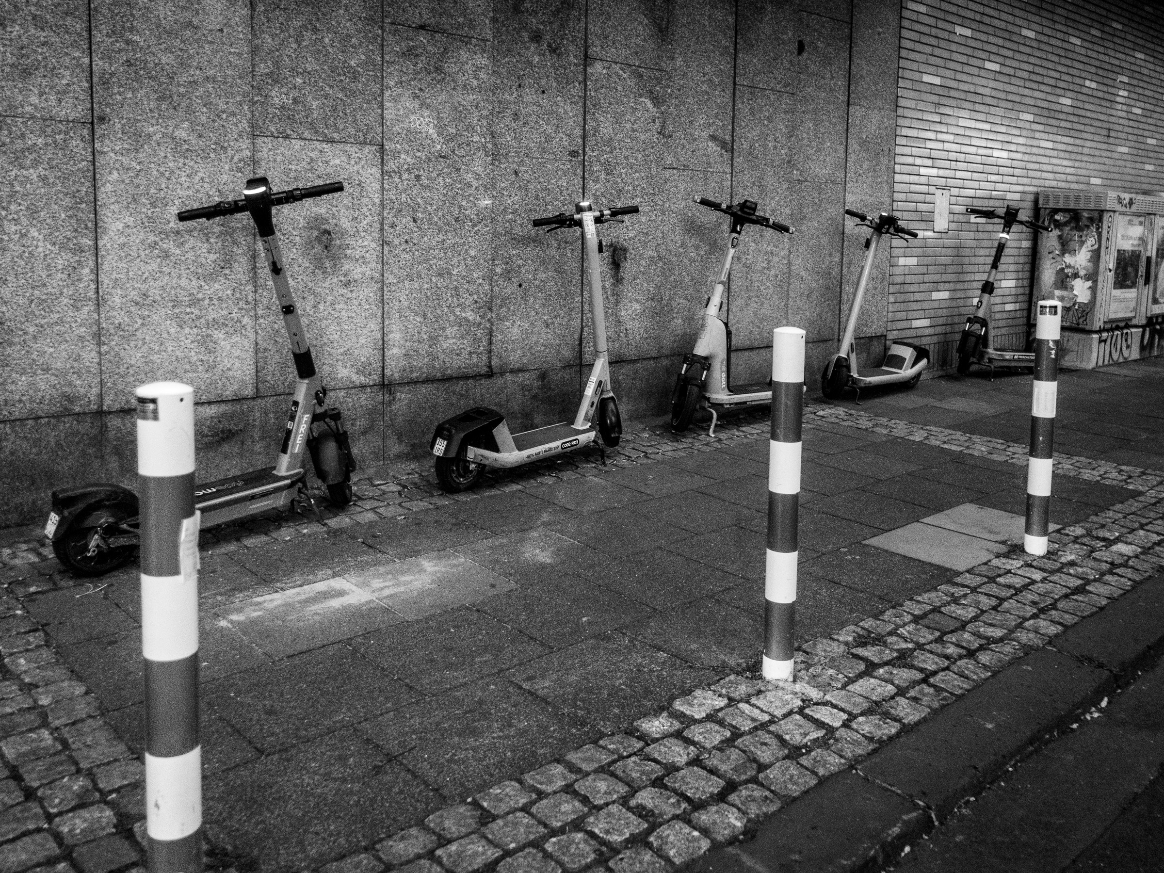 Row of parked e-scooters against a stone wall at night, Lohsestraße, Cologne