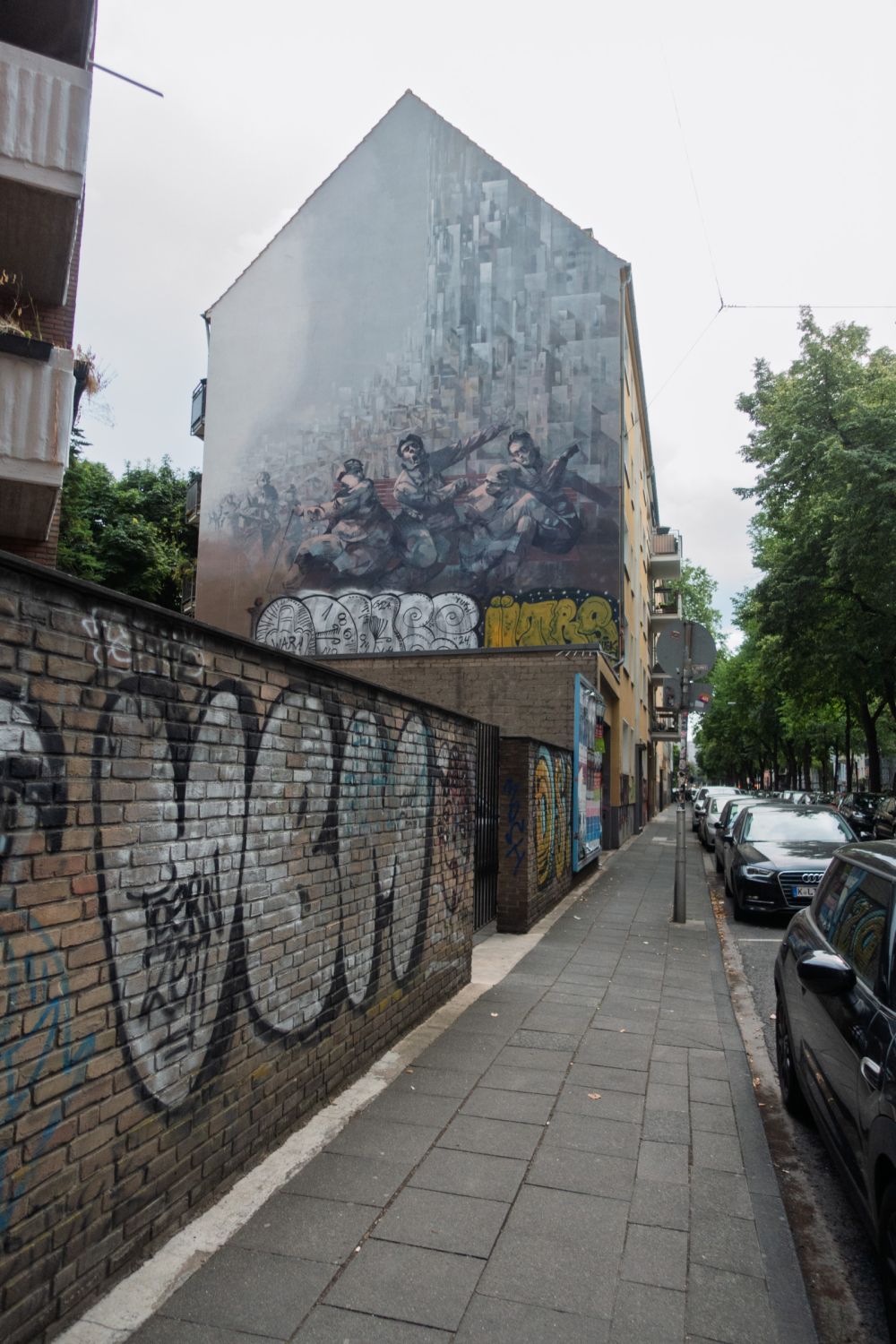 Painted gable mural above a graffiti-covered brick fence, Ehrenfeld, Cologne