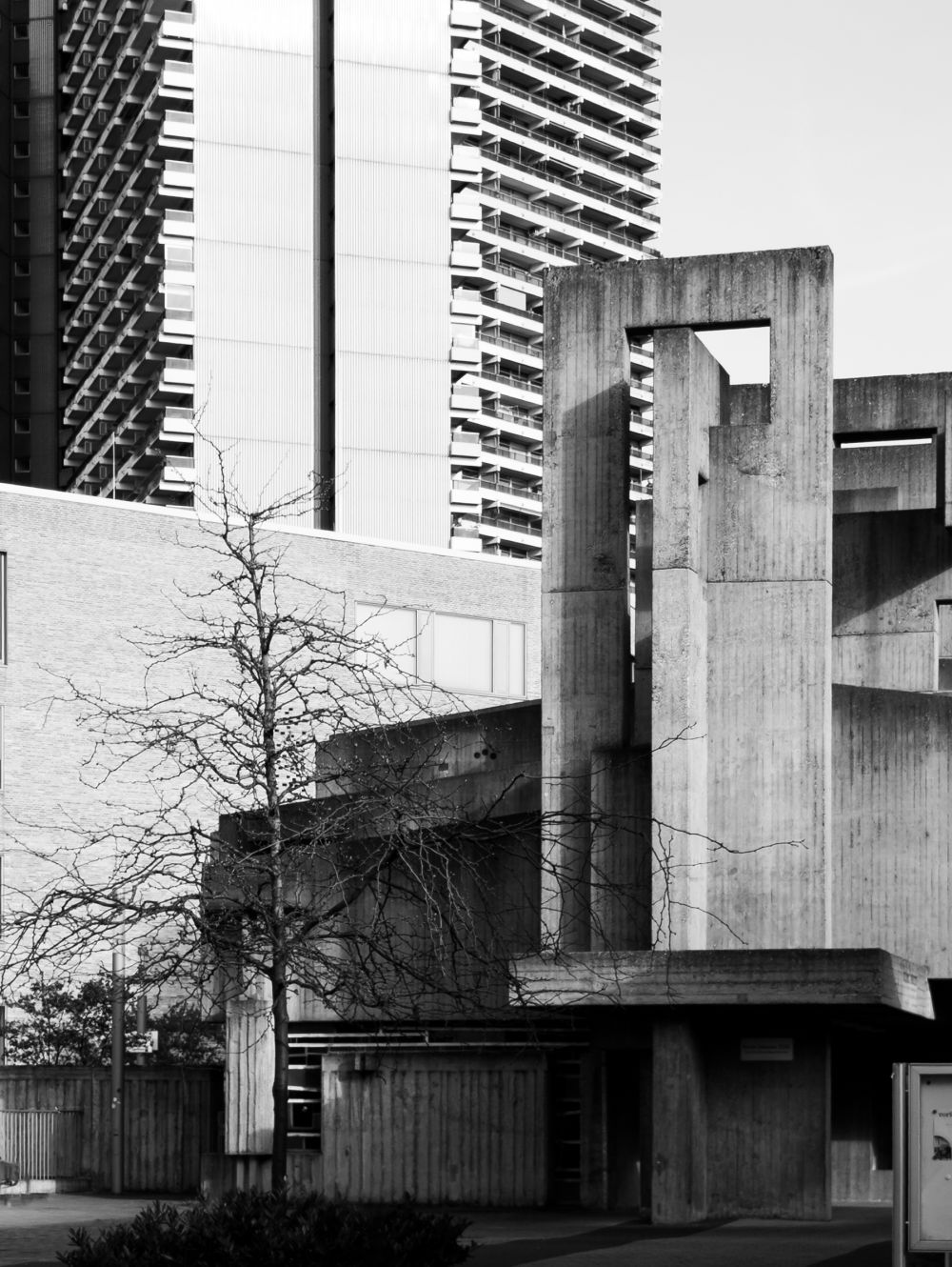 Kirche St. Johannes XXIII Köln — brutalist church entrance with bare tree and Uni-Center tower behind