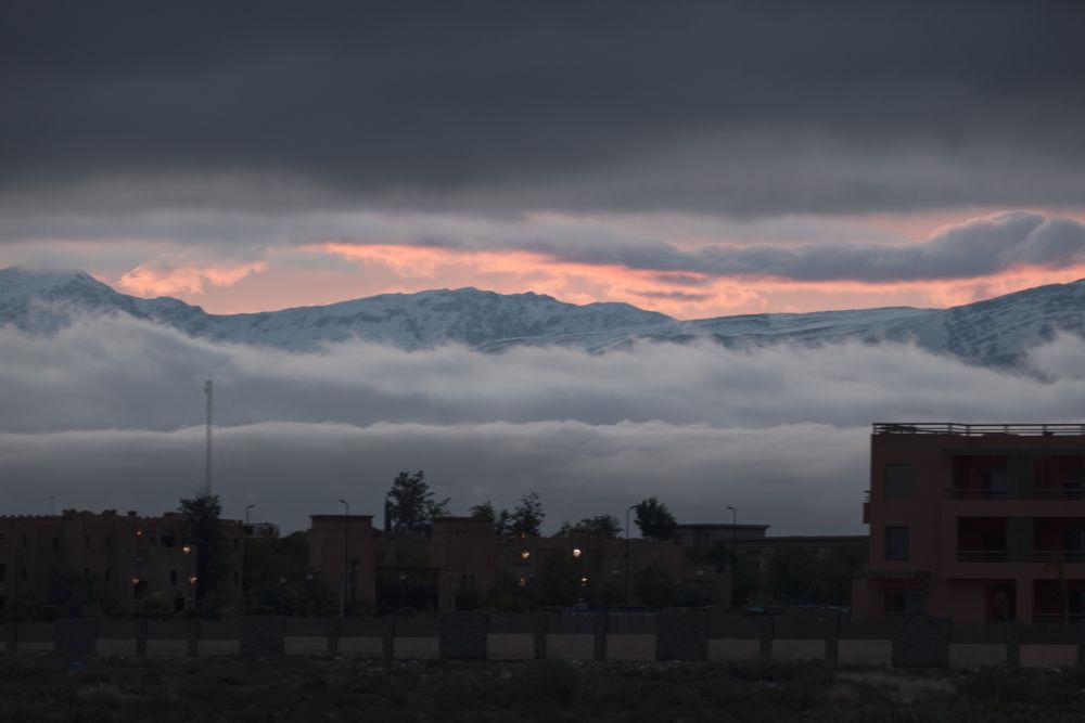 Town at dusk with dramatic clouds over the Atlas Mountains, creating a moody atmosphere.