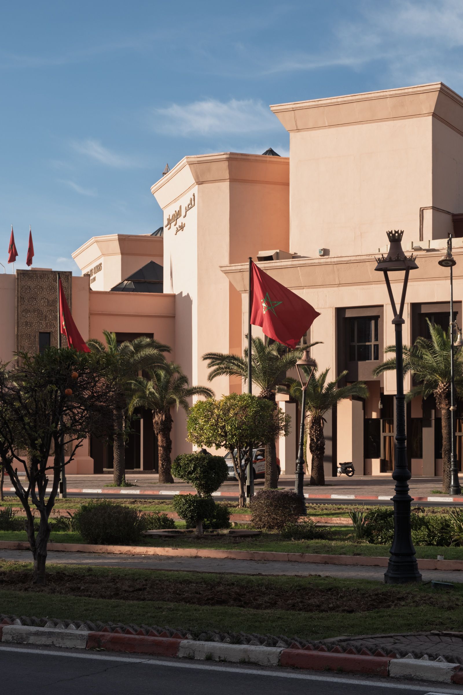 Front view of Palais des Congrès, Marrakech, with its iconic signage and Moroccan flags under blue skies.